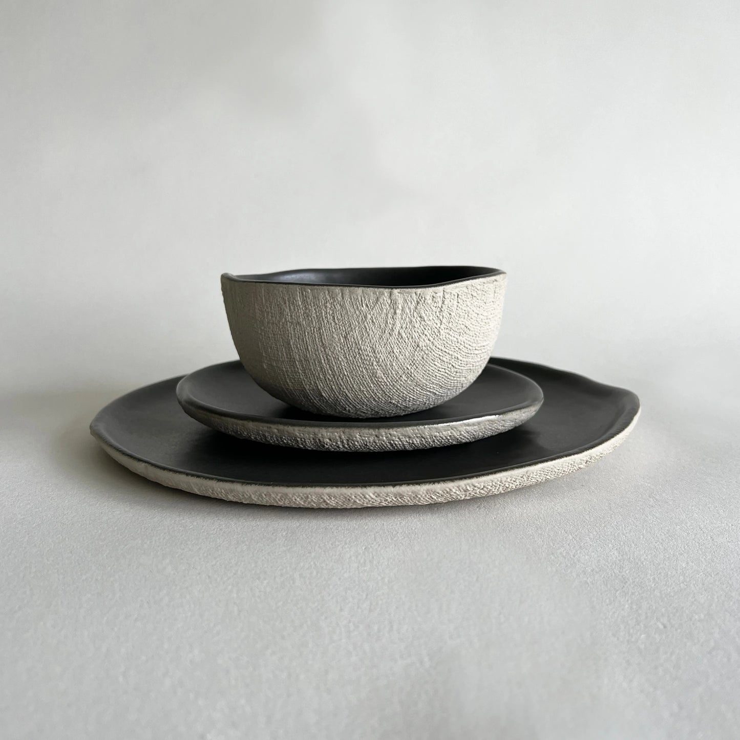 A set of 3 ceramic plates and matching bowl. The set includes matte charcoal dinner plate, dessert plate, and breakfast or soup bowl, finished with beige texture.