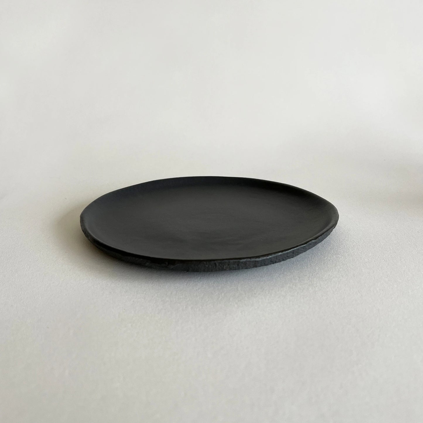 Side matte black ceramic plate with a slightly textured and uneven, rustic rim.