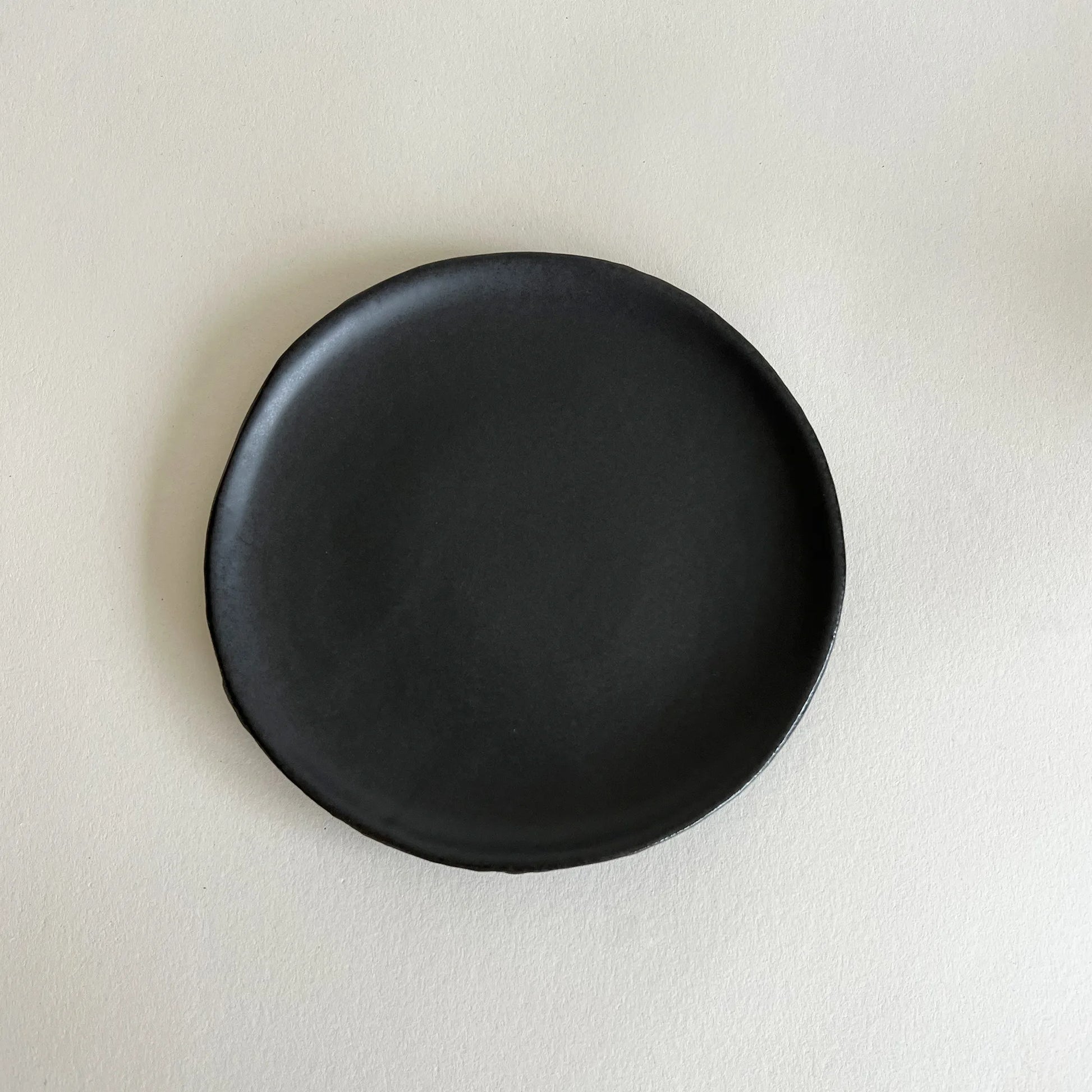 matte deep black ceramic side plate with a slightly irregular hand-painted edge, 