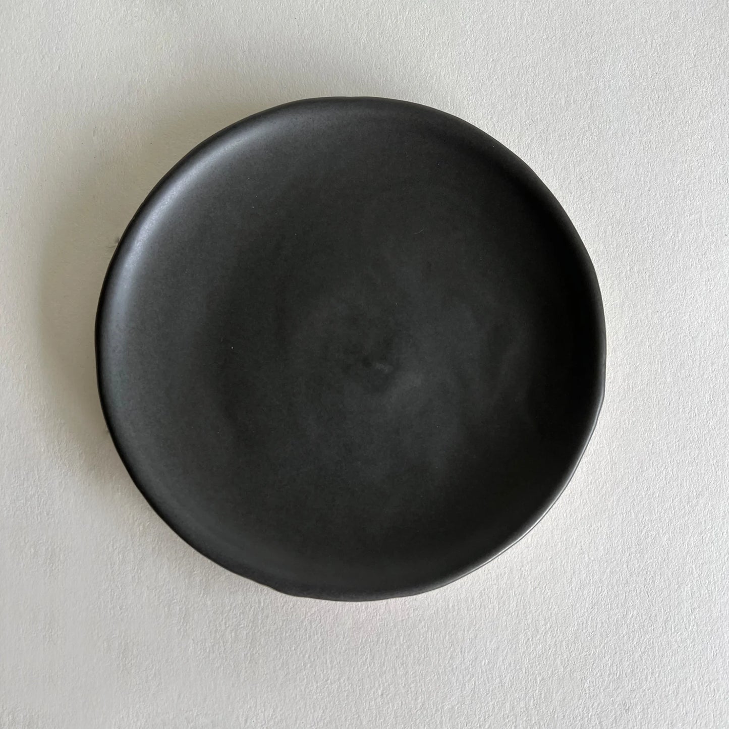 Handcrafted ceramic matte charcoal side plate with organic texture at the bottom.