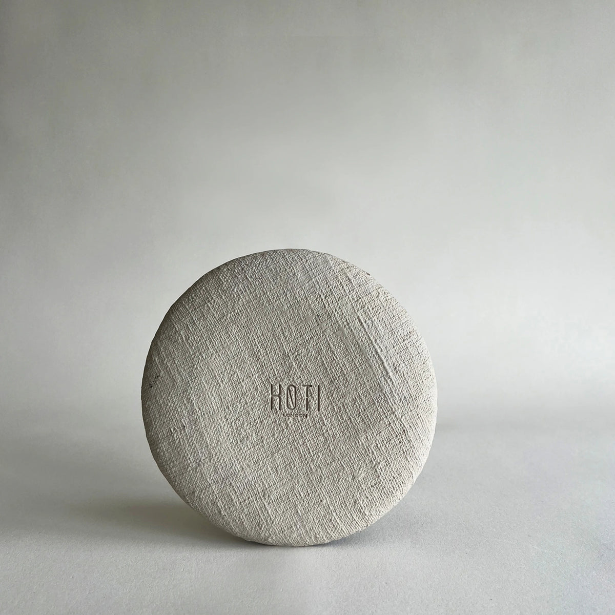 A round, textured beige side ceramic plate, showcasing the raw and matte finish.