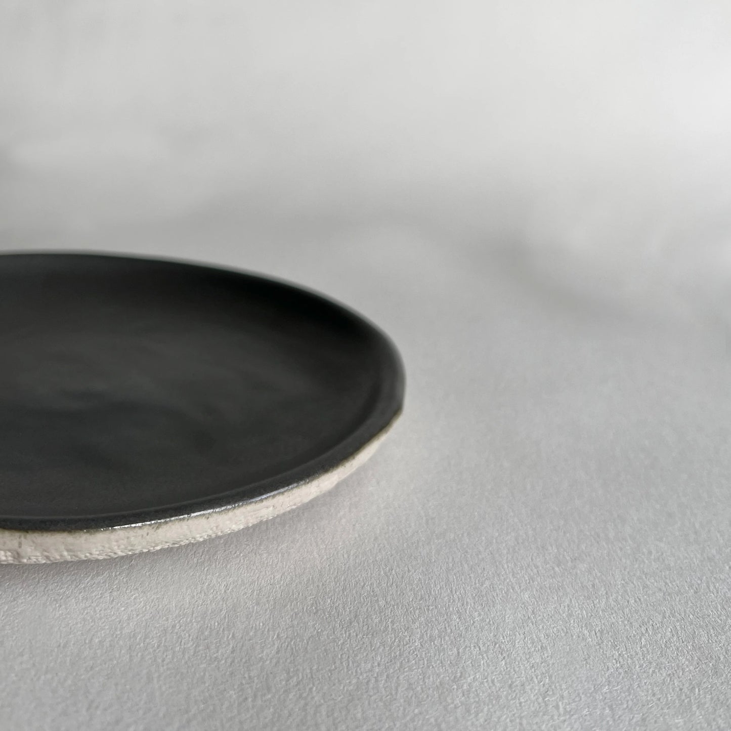 Close up of handmade ceramic side plate in dark grey colour in matte finish, contrasted with beige organic texture.