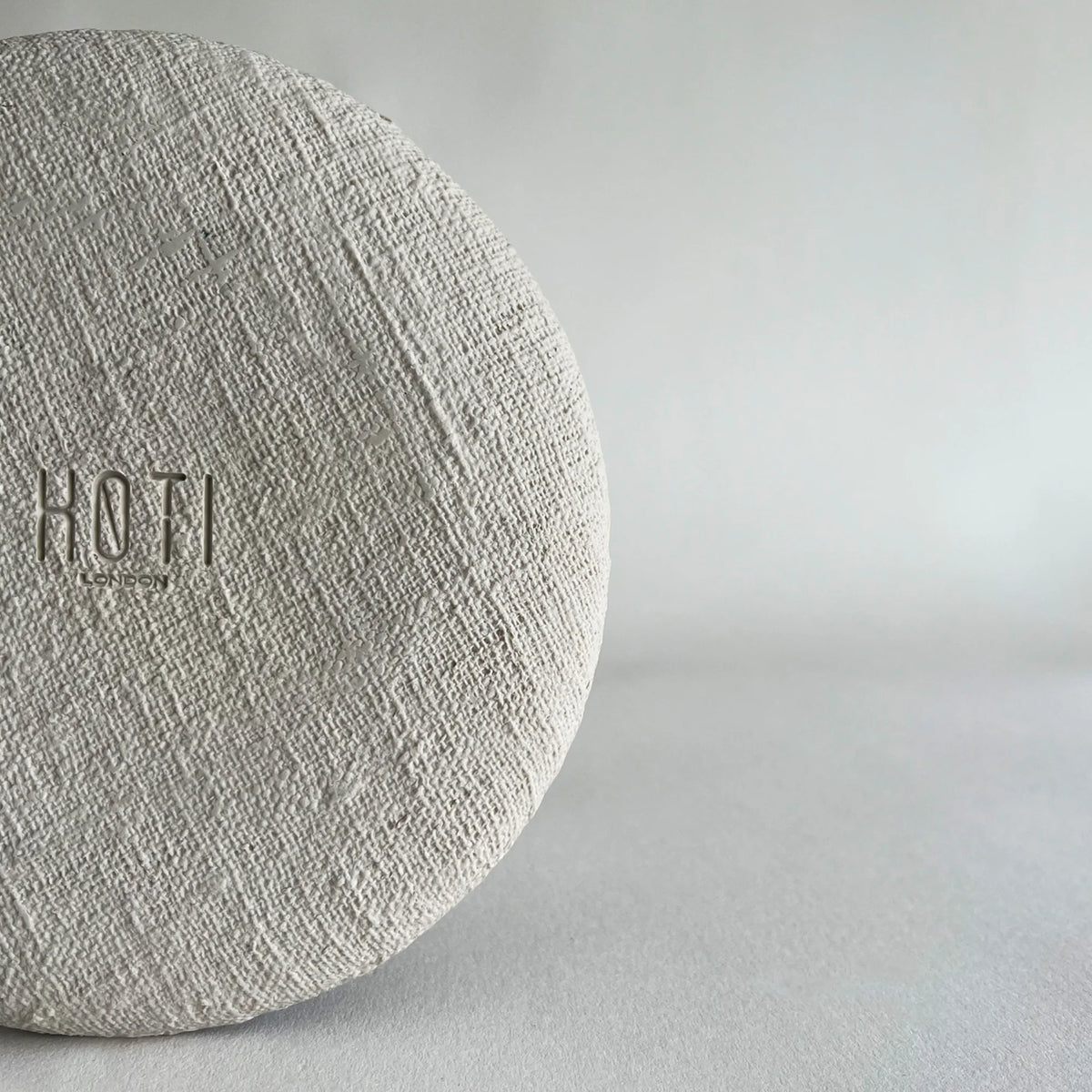 A close-up of a round, textured light beige ceramic plate, showcasing organic woven texture and finish. 