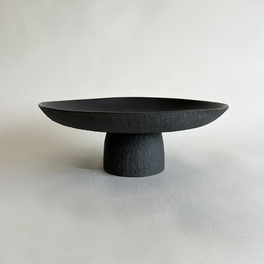 A modern matte black ceramic pedestal tray with a wide, shallow oval bowl and a textured cylindrical base.