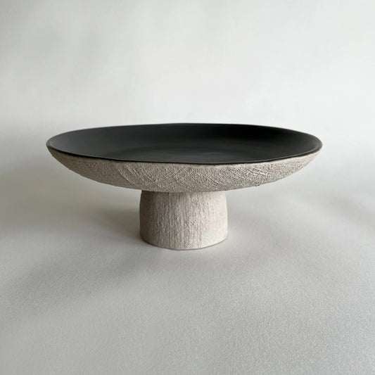 Rustic handmade ceramic pedestal serving platter or decorative bowl in satin dark grey colour contrasted with organic woven texture.