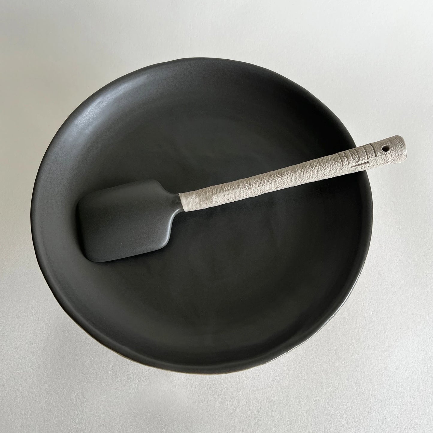 Set of matte beige and charcoal ceramic serving tray and matching textured serving spoon.