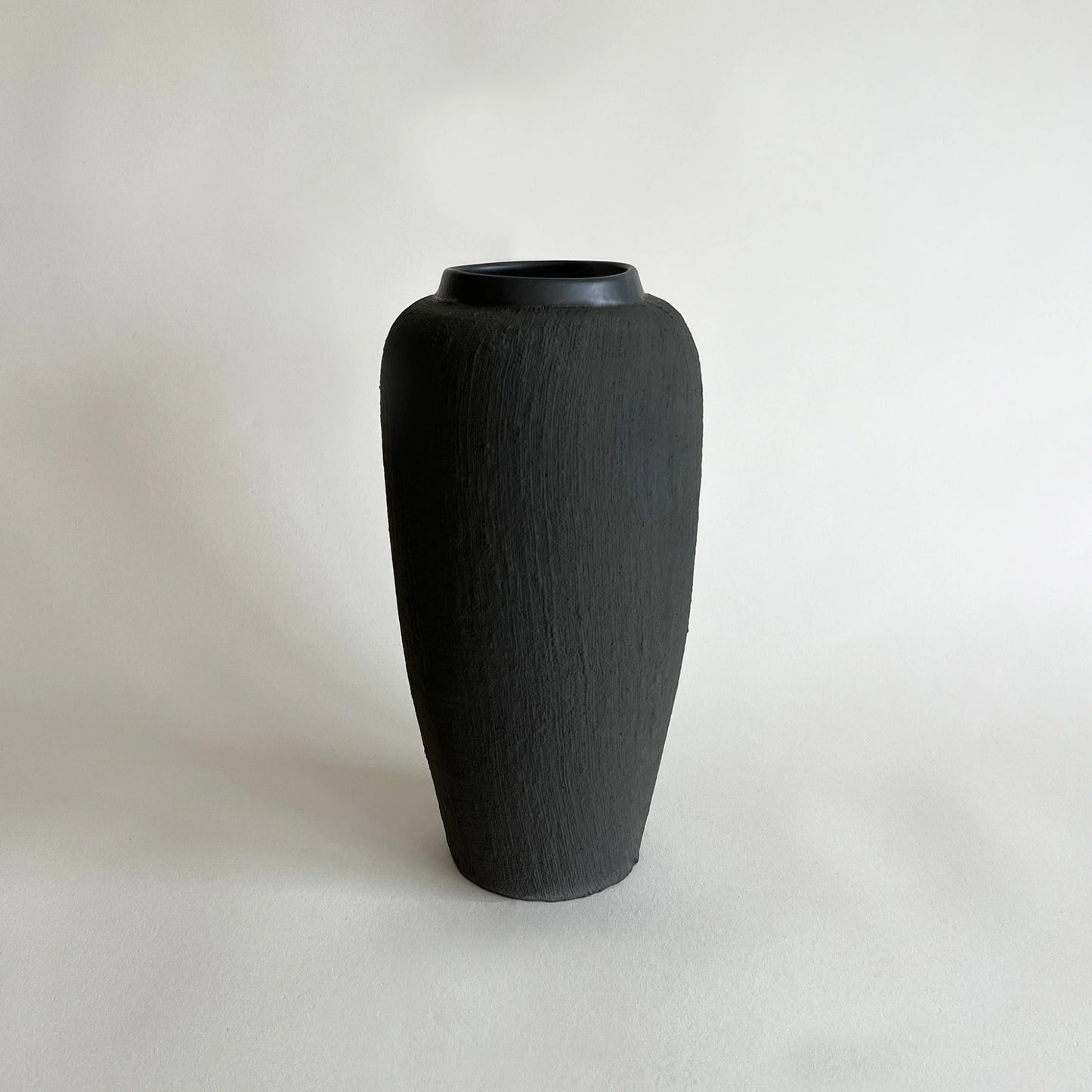 A tall matte black textured ceramic vase with a flared rim, with woven linen organic texture.