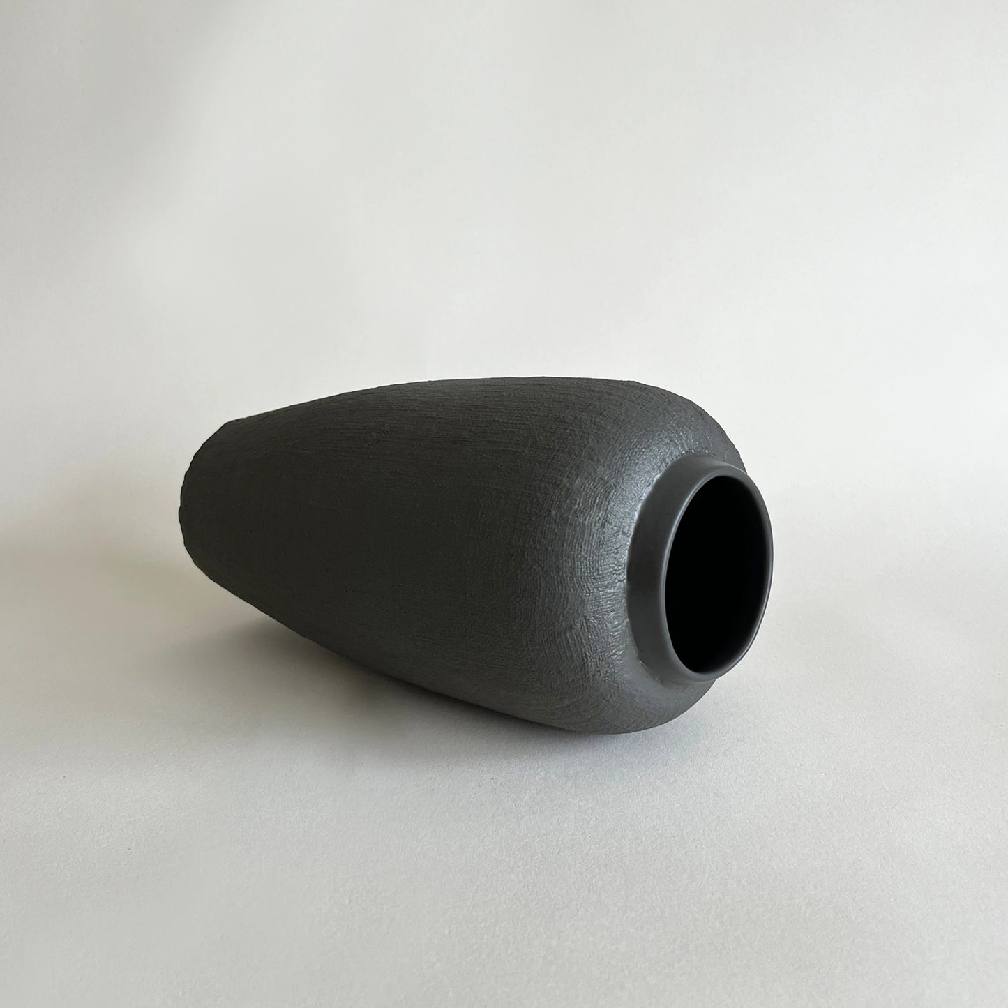 A tall matte black ceramic vase with a textured organic jute finish.