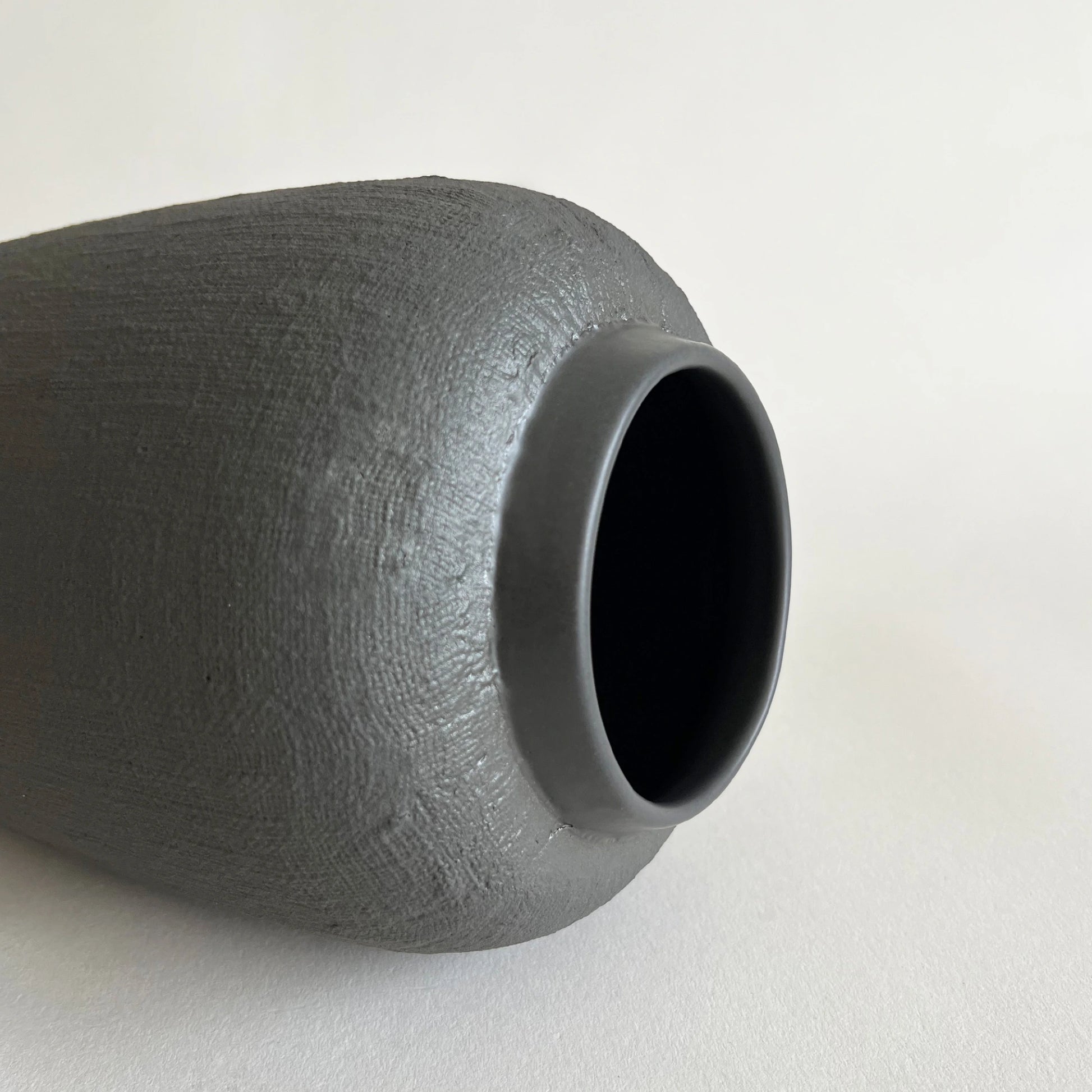 A close-up of a dark grey textured ceramic vase with a matte finish and a wide flared rim, close up of linen jute organic finish.