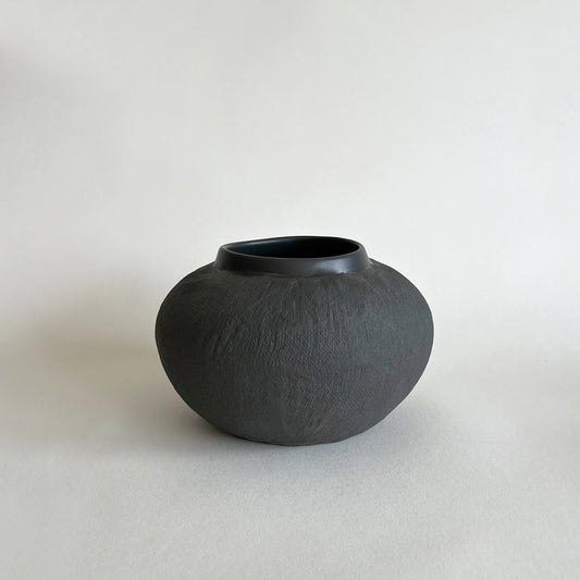 A matte black ceramic vase with a textured, hand-painted finish and a slightly asymmetrical rim.