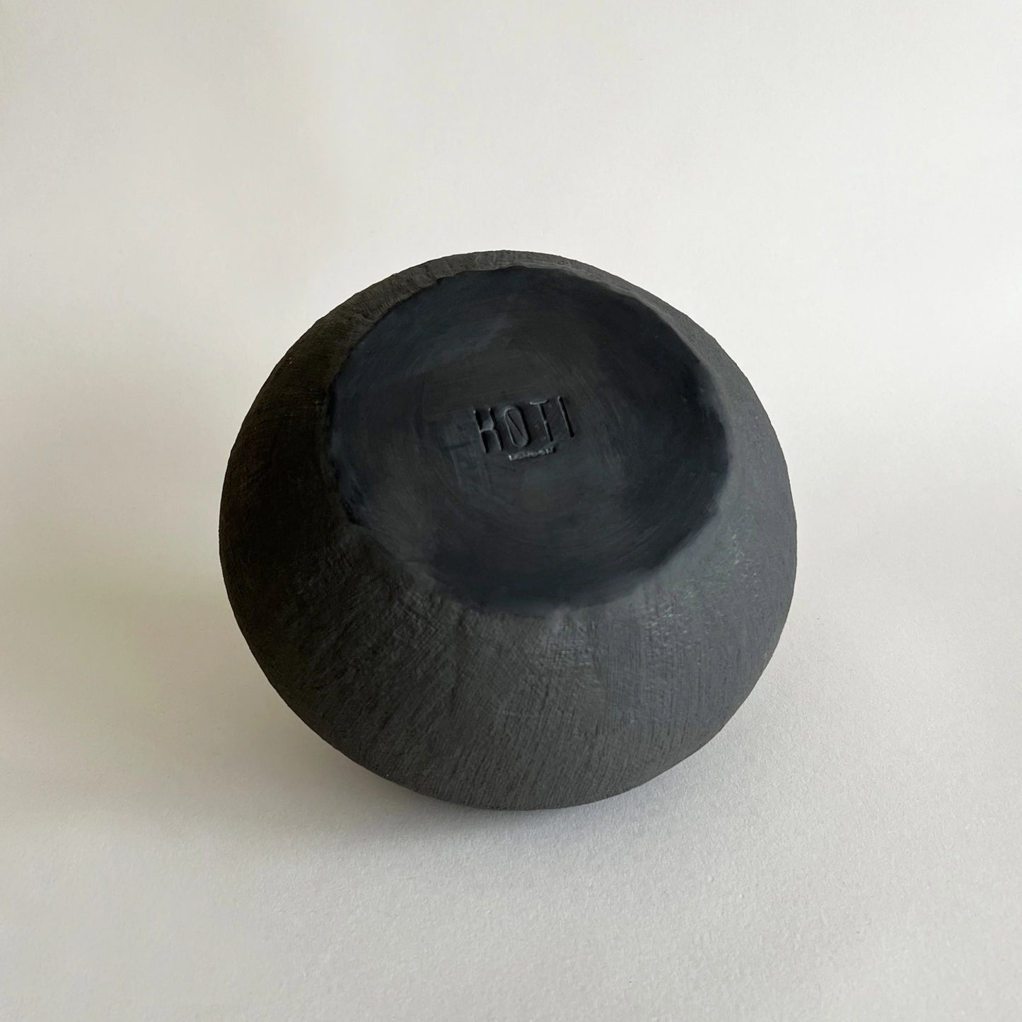 Round, hand-carved dark charcoal vase with a matte finish, close up of organic texture.
