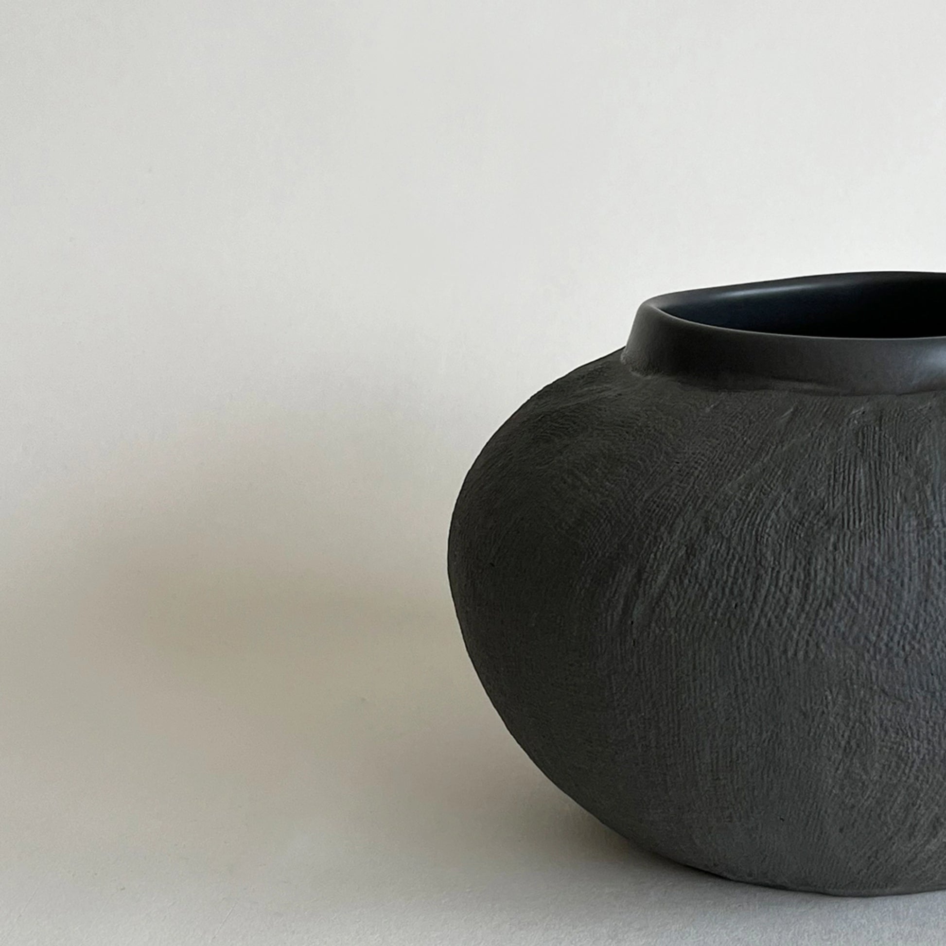 A dark charcoal textured ceramic vase with a wide flared rim, showcasing the close up of organic textured finish.