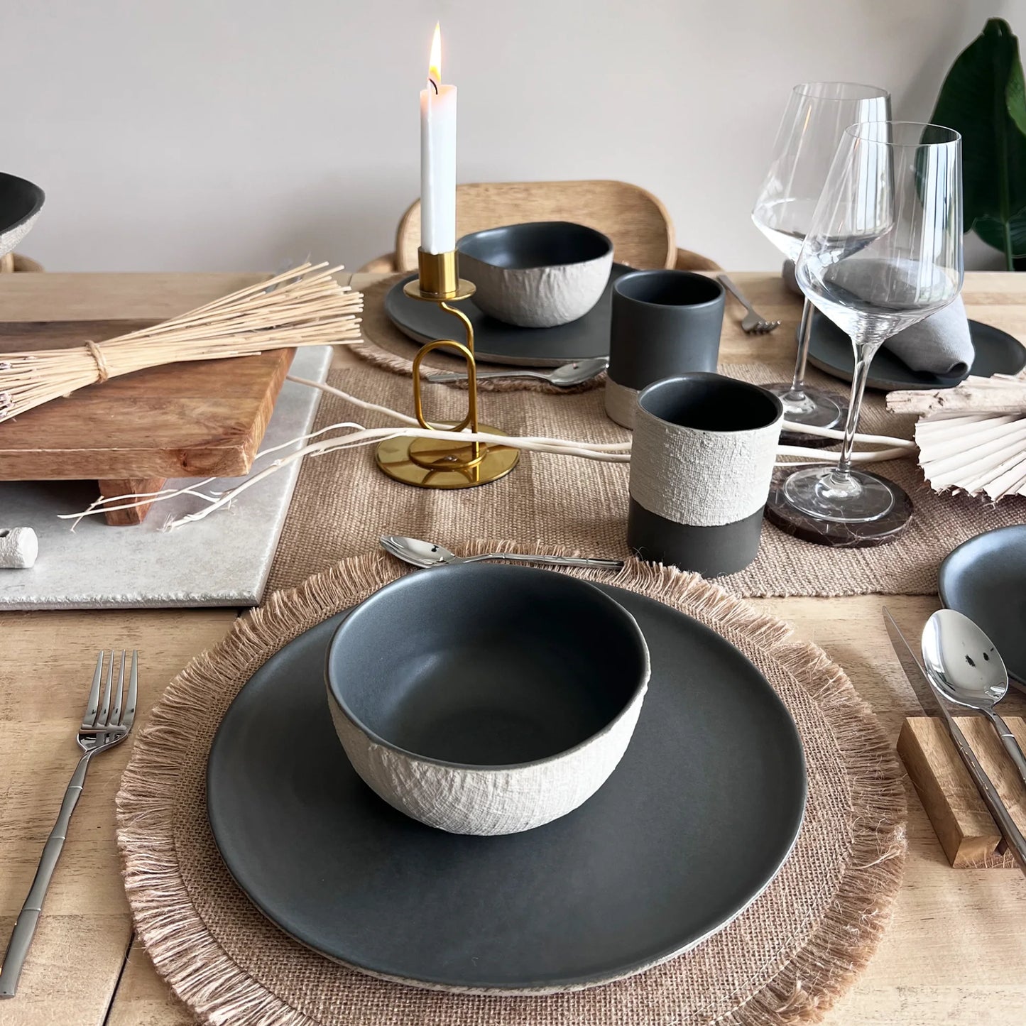 Dining table setting with matte grey ceramic bowls, plates and mugs,  with beige textured contrast finish. 