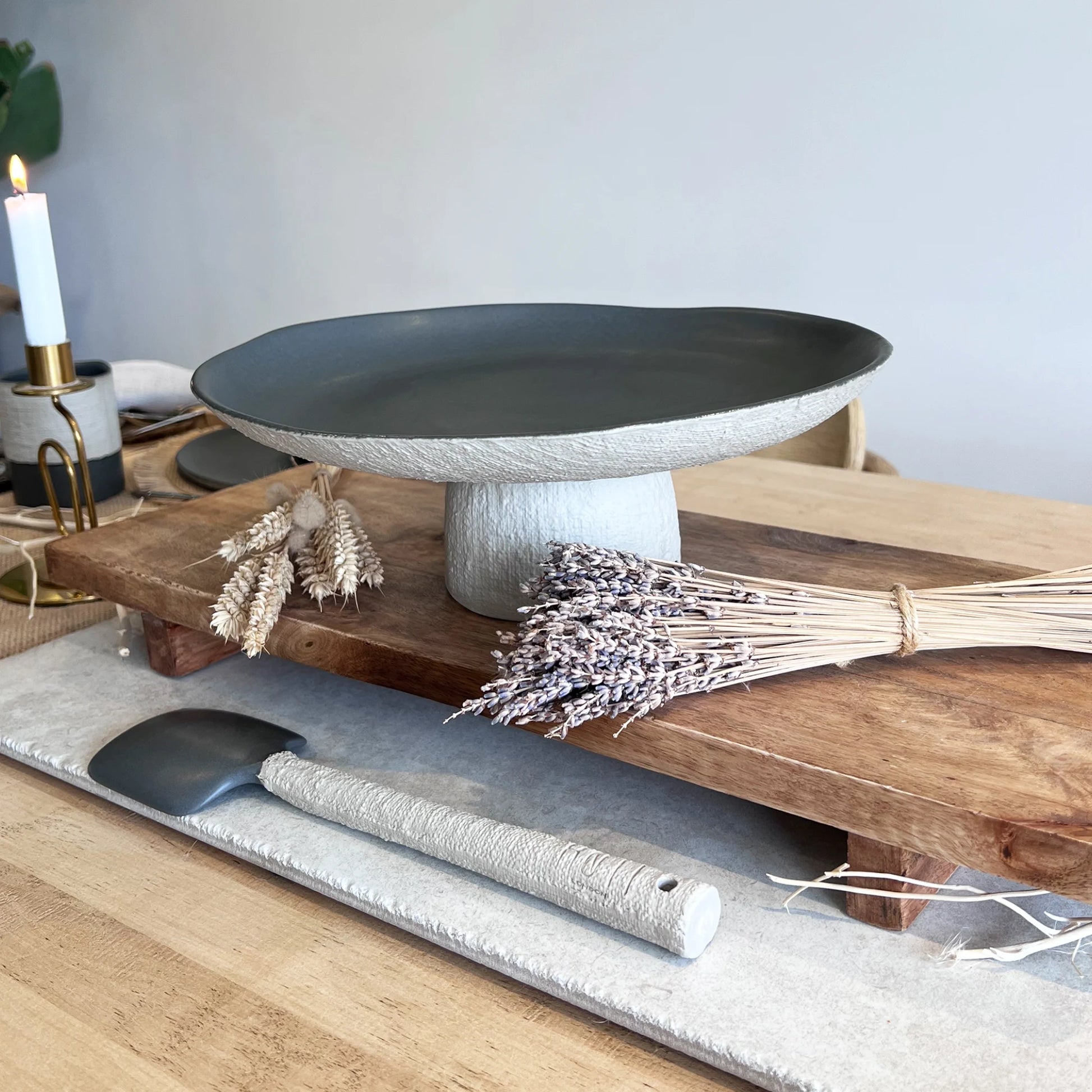 Decorative setting with a dark grey ceramic serving platter, with matching textured serving spoon on wooden board, on a light wooden surface.