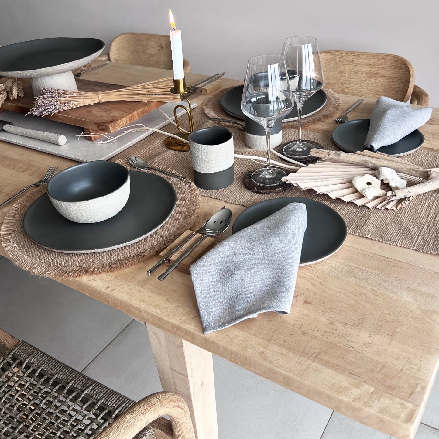 Dining table set with matte dark grey plates, charcoal bowls, and textured cups on a wooden table, showcasing rustic style.