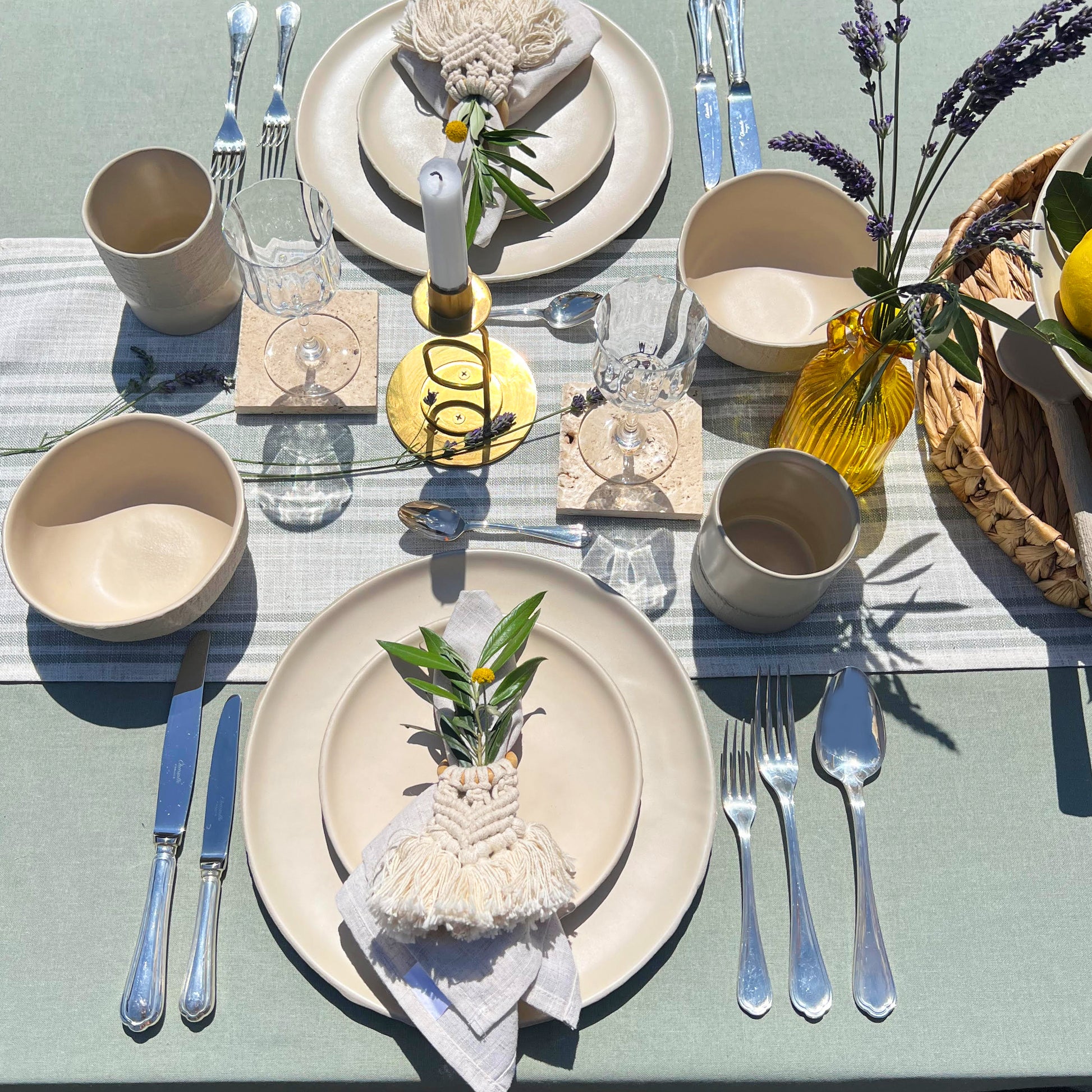 Elegant table setting with beige plates, silverware, and decorative elements on a light green tablecloth.