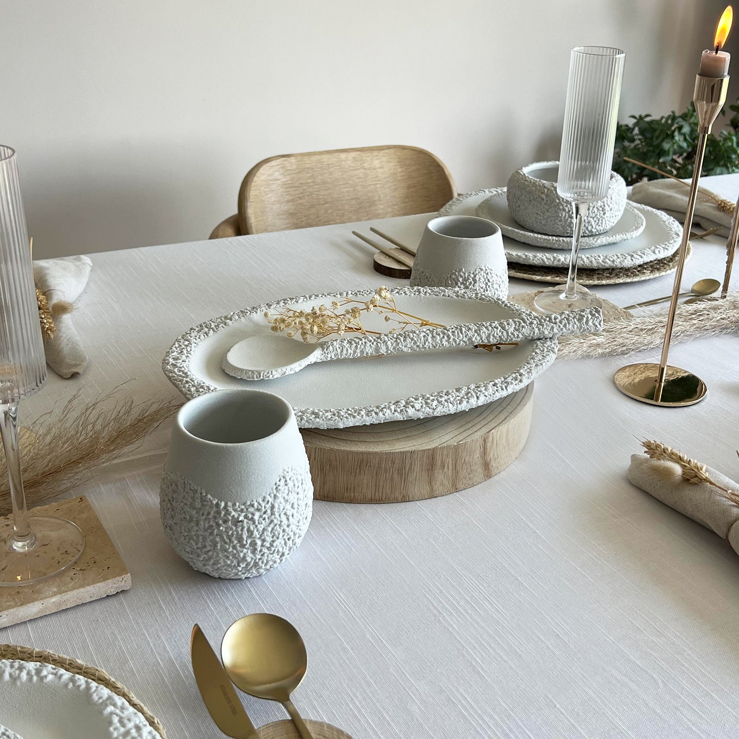 Elegant dining table setting with white ceramic centrepiece, gold cutlery, and rustic decorative elements.