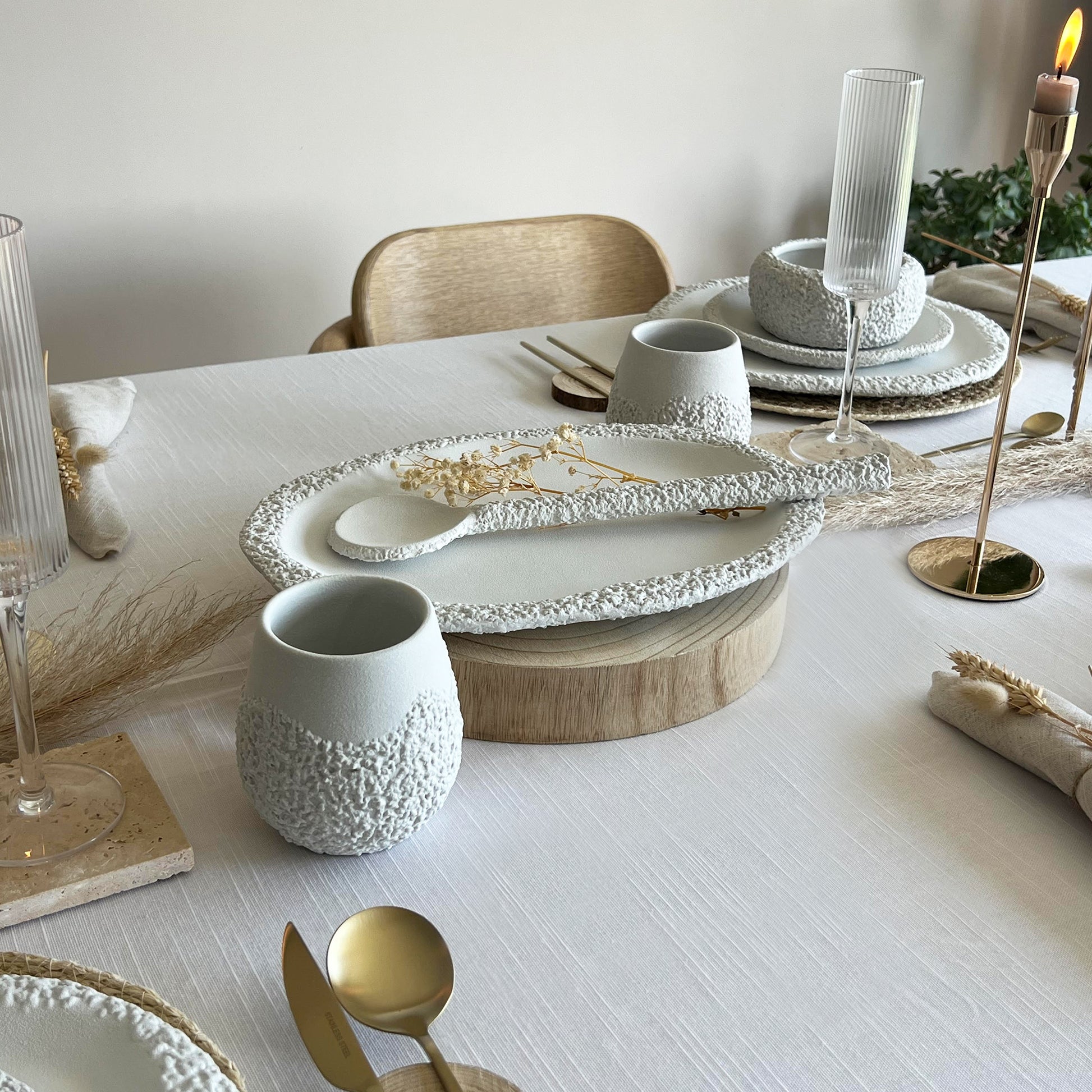 Elegant dining table setting with white ceramic centrepiece, gold cutlery, and rustic decorative elements.