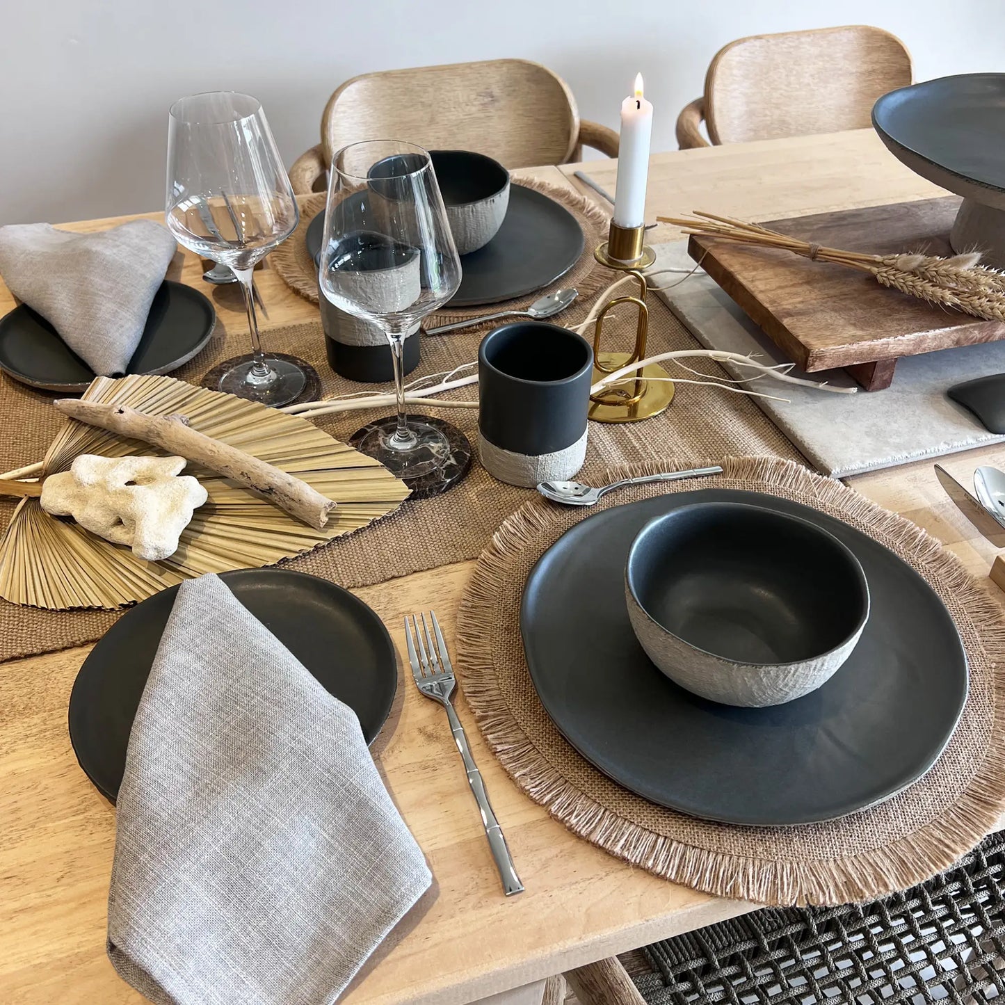 Dining table set with ceramic matte beige and charcoal dinner plates, salad plates, soup bowls and mugs on a wooden table.