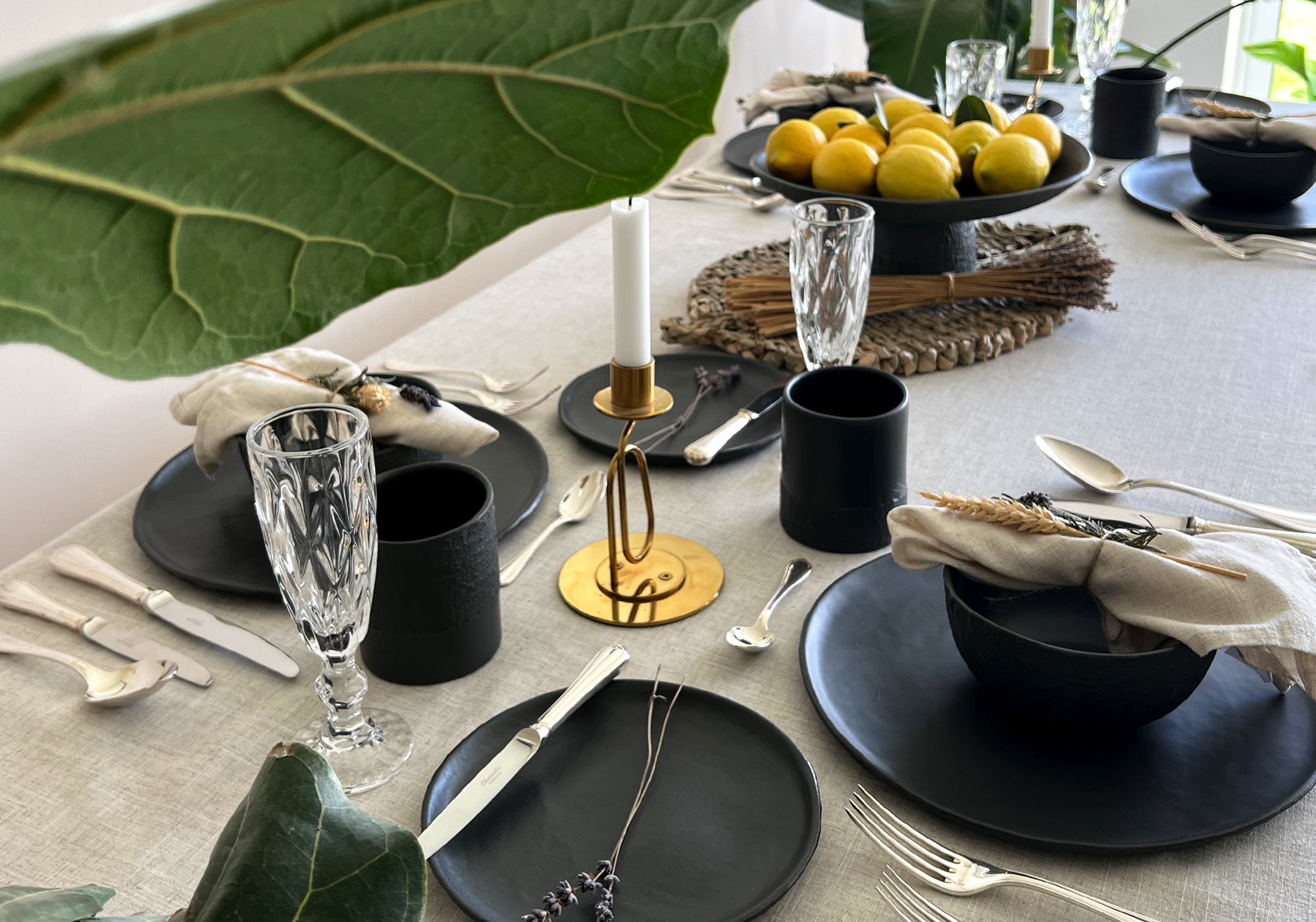 Elegant table setting with black plates, cups, and silverware on a light linen tablecloth.
