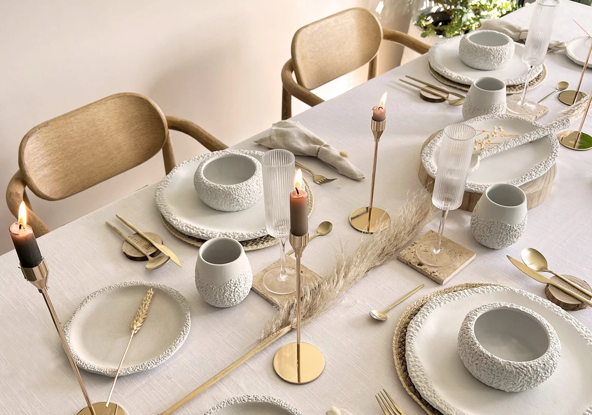 Elegant dining table setting with white ceramic dinnerware set, gold cutlery, and candles on a white linen tablecloth