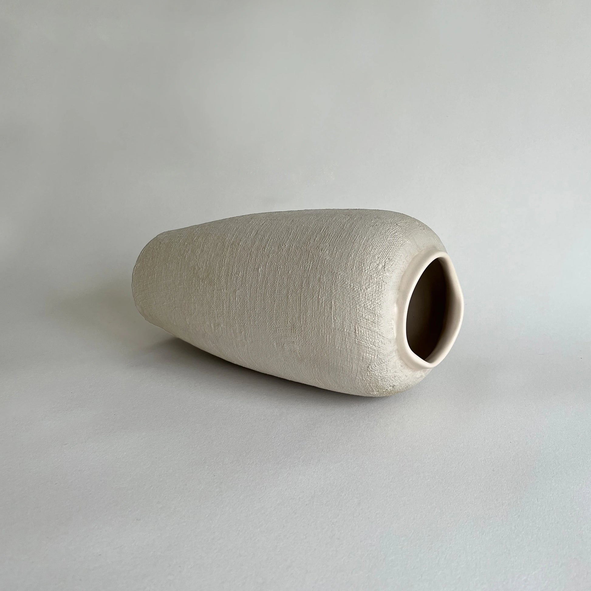A tall handcrafted textured ceramic vase showcased with organic linen texture in earth beige colour with matte finish.