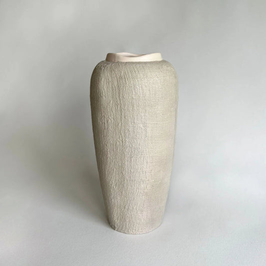 A tall, beige handmade textured ceramic vase with a flared rim, with organic linen texture.