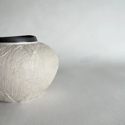 A textured ceramic vase with a ribbed, woven-look body in a light beige and a contrasting dark grey rim.