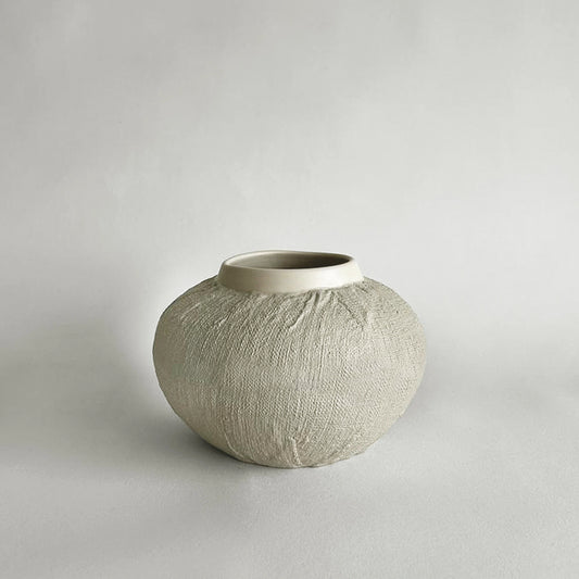 Handmade Textured ceramic vase with linen organic finish in medium size and warm beige colour on a plain background.